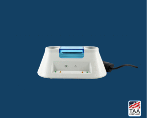 Riester ri-charger L desktop charging station with white base and vertical dual-slot mount, positioned centrally on blue background; TAA Compliant box featuring American flag visible in lower right corner.