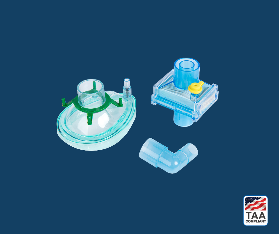 Pall VMPKPED breathing filter — shown in angled profile view to highlight translucent housing, dual coaxial port configuration, ribbed filtration chamber, and integrated pediatric mask interface; positioned centrally on blue background with TAA Compliant box featuring American flag visible in lower right corner.